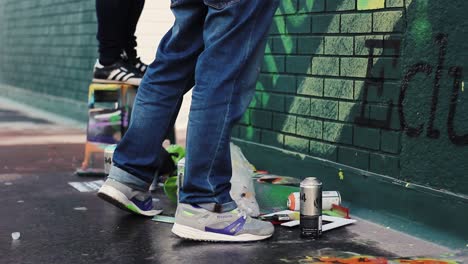 Low-shot-of-two-spray-paint-artists-feet-as-they-collaborate-spraying-a-mural