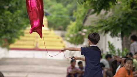 Burmesisches-Kind,-Das-Mit-Einem-Roten-Hai-Ballon-Auf-Der-Straße-In-Mandalay-Spielt