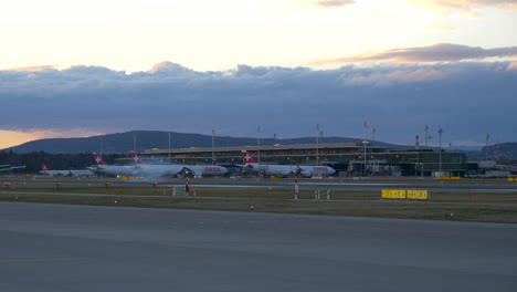 Airliner-aircraft-landing-on-airport-runway-in-front-of-terminal-during-evening-twilight,-dusk