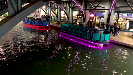 Die-Hellen-Und-Farbenfrohen-Neon-LED-Lichter-Der-Flussboote-Auf-Dem-San-Antonio-Riverwalk,-Deren-Lichter-Auf-Der-Oberfläche-Zu-Tanzen-Scheinen