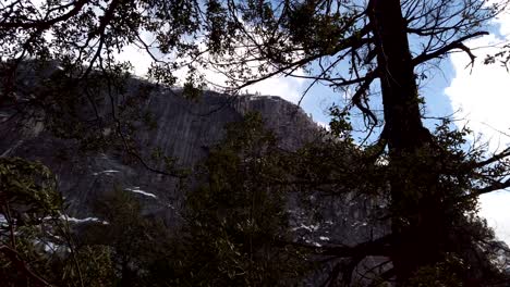 Moving-slowly-through-the-trees-while-looking-up-at-the-tree-lined,-snow-covered-cliff-faces-along-Mist-Trail-in-Yosemite-National-Park