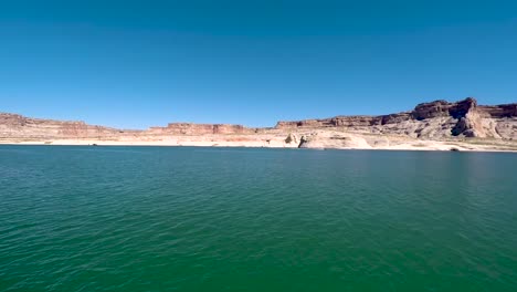 Pan-across-the-sandstone-buttes-from-the-turquoise-waters-of-the-shore-of-Lake-Powell,-Page-Arizona