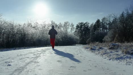 A-man-is-jogging-on-a-snowy-and-ice-covered-forest-path-during-a-beautiful-sunny-and-cold-winter-afternoon-towards-the-camera