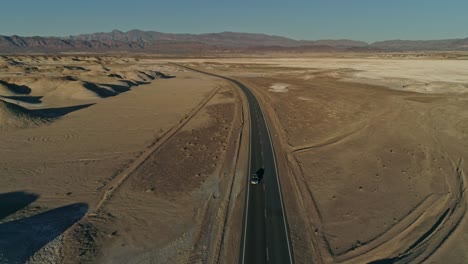 Alta-Vista-Aérea-Siguiendo-Una-Curva-De-Carretera-Con-Camiones-En-Movimiento-En-El-Desierto