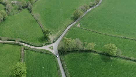 Top-down-drone-shot-of-a-silver-car-traveling-around-a-country-lane,-slowing-down-for-a-quiet-junction