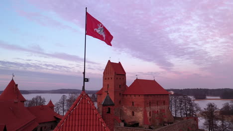AERIAL:-Reveal-Shot-of-Waving-Lithuanian-Flag-with-White-Vytis-on-a-Red-Field-on-the-Top-of-Trakai-Island-Castle-Gate-Tower