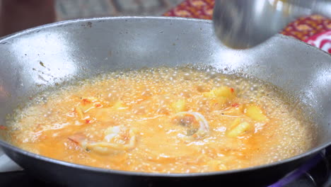 Nahaufnahme-Eines-Kochs,-Der-Mit-Einem-Stahlwok-Ein-Thailändisches-Rotes-Currygericht-Mit-Frischen-Garnelen-Und-Ananas-Zubereitet