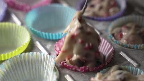 Scooping-muffin-batter-with-tasty-fruit-into-colorful-wrappers-in-metal-baking-tray-close-up