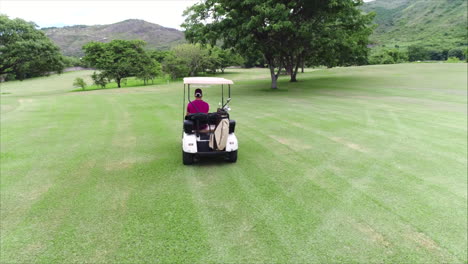 AERIAL:-Side-shot-of-guy-driving-golf-cart-at-golf-course