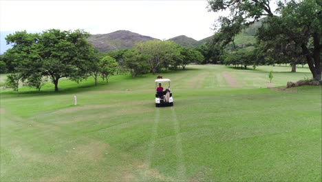 AERIAL-SLOW-MOTION:-Following-guy-driving-golf-cart-at-golf-course