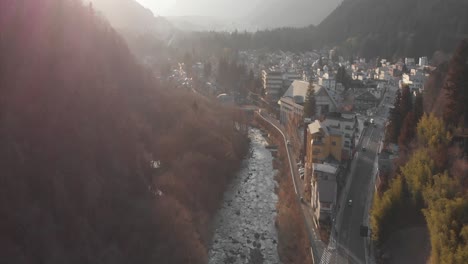 Drone-flight,-over-small-Japanese-town-of-Nikko,-misty-background-during-golden-hour-with-rays-shining-showing-silhouettes-of-mountains-in-the-background-and-a-river-running-through-the-middle