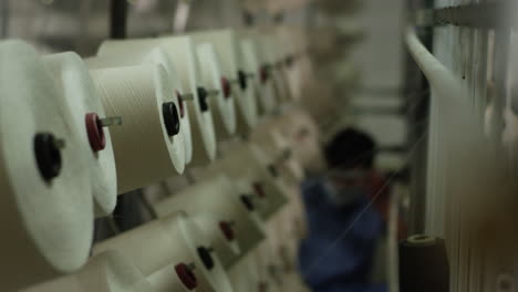 Factory-worker-checking-a-smooth-operation-of-cotton-warpers-bobbins-of-an-automated-textile-winding-machinery-in-a-factory-in-China