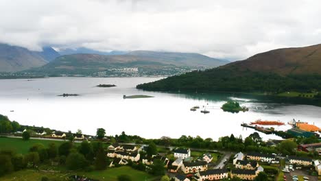 Cinematic-panning-drone-shot-of-scottish-lakeside-village-with-misty-mountains-in-background