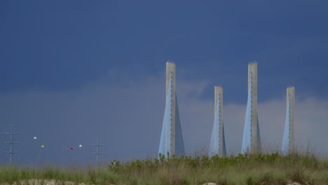 Time-lapsed-shot-of-bridge-and-power-lines-with-dunes-in-foreground-and-dramatic-clouds-in-sky