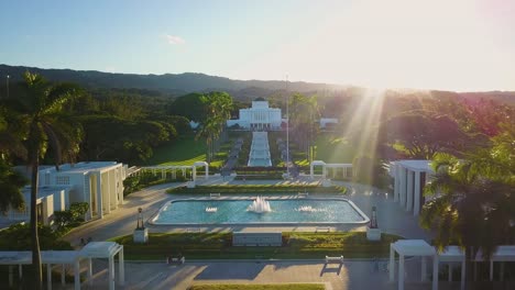Drone-Shot-flying-in-between-palm-trees,-over-the-beautiful-temple-grounds,-towards-the-Laie-Hawaii-Mormon-Temple