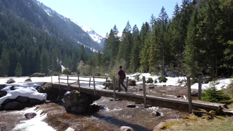 Still-shot-of-a-young-man-walking-over-a-bridge-on-a-valley-in-the-Swiss-Alps