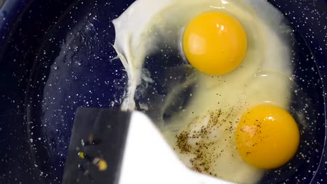 Two-eggs-cooking-in-frying-pan-with-added-pepper-top-view