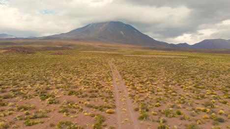 Aerial-cinematic-shot-following-a-dirt-road-showing-Lascar-Volcano-in-the-Atacama-Desert,-Chile,-South-America