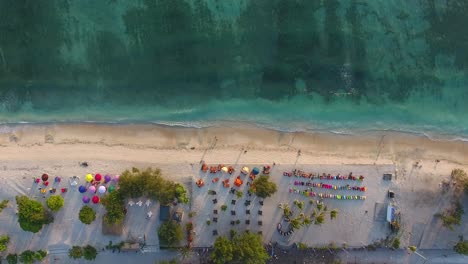Aerial-top-down-view-of-Gili-Trawangan-beach-island-at-sunset,-bean-bags-and-parasols-on-the-sandy-beach,-people-watching-the-sunset-and-enjoying-their-vacation,-holiday