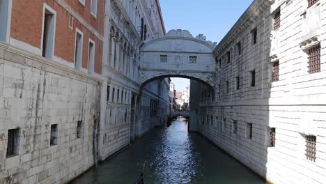 Venice-Italy-lonely-touristic-Gondola-in-a-Canal-passing-under-a-Bridge-on-a-sunny-day-Venezia-City