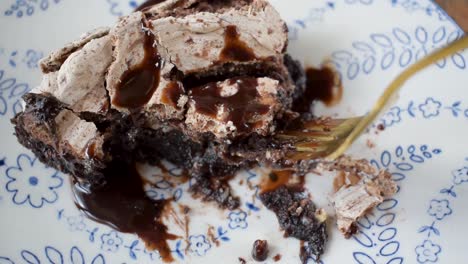 Eine-Gabel-Beißt-Aus-Einer-Gebackenen-Brownie-Dessertscheibe,-Garniert-Mit-Baiser-Und-Beträufeltem-Schokoladensirup