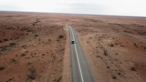 Aerial:-Drone-shot-tracking-a-vehicle-driving-down-an-empty-road-in-the-Australian-outback-towards-the-horizon-near-Broken-Hill,-Australia