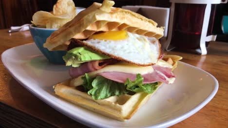 Waffle-sandwich-with-egg,-bacon,-avocado,-ham-and-cheese-with-sidedish-chips