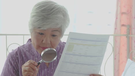 Elderly-woman-using-a-magnifying-glass-to-reading-through-the-lens-to-handheld-document-as-her-eyesight-deteriorates-with-age