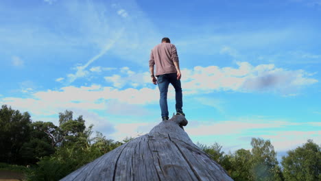 Man-walking-on-a-fallen-tree-trunk,-then-standing-at-the-top-looking-into-the-distance
