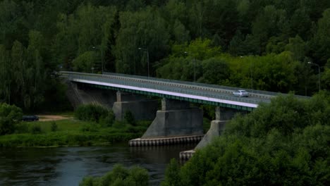 Moody-shot-of-car-driving-on-a-bridge-with-green-forest-around-it