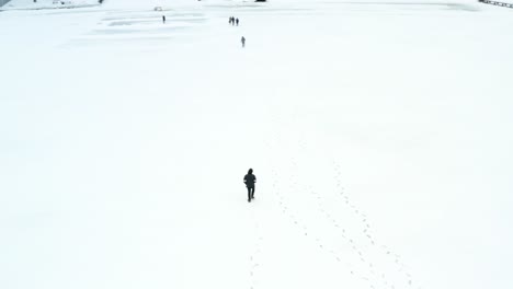 An-aerial-drone-shot-orbiting-a-person-walking-in-the-middle-of-a-frozen-lake-in-the-winter