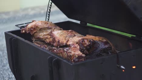 Barbecuing-a-juicy-pig-in-a-black-metal-grill-outdoors,-slow-motion