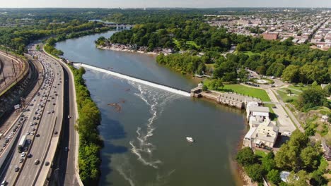 Beautiful-high-aerial-descending-shot-above-Schuylkill-River,-with-express-traffic,-green-park,-and-Philadelphia-residential-areas-during-sunny-summer-day