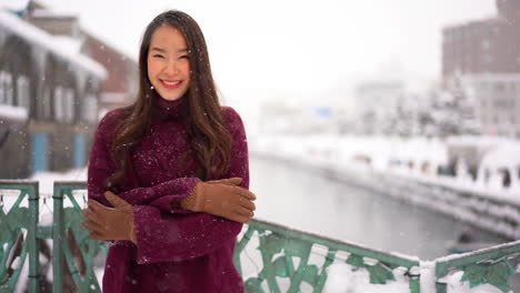 Static-shot-of-a-Asian-woman,-standing-cold-and-smiling,-in-the-snowfall,-in-Otaru,-Hokkaido,-Japan