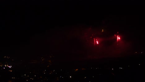 Celebration-with-red-fireworks,-over-a-mountain-town,-at-night