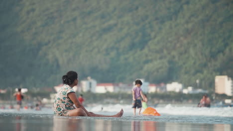 Woman-Sitting-on-Beach-Shoreline-Watching-Kids-Swim-and-Play-in-Vietnam
