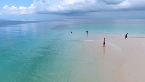 Fliegen-über-Menschen-Und-Booten-Auf-Einer-Tropischen-Sandinsel,-Umgeben-Von-Kristallklarem-Türkisfarbenem-Wasser