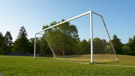 Low-angle-shot-of-a-soccer-net-and-field-on-a-sunny,-summer-morning
