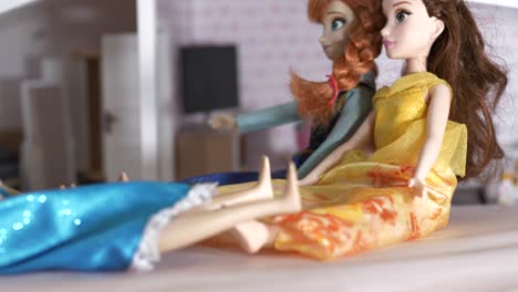 Sliding-shot-of-sitting-barbie-dolls,-with-doll-house-in-blurry-background