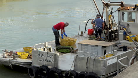 Medium-view,-Oyster-farmers-working-on-the-deck-of-their-flat-bottomed-boat-after-an-outing-to-sea,-port-of-Saint-Trojan-les-Bain,-island-of-Oleron