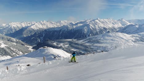 Snowboarder-on-a-slope-enjoying-the-view-over-a-valley-and-snow-covered-mountains