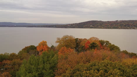 aerial-drone-dolly-out-over-the-autumn-colored-tree-tops,-towards-the-Hudson-River-on-a-cloudy-day-at-Croton-Point-Park-which-was-empty