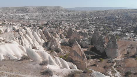 Ascending-wide-aerial-view-of-the-amazing-rock-formations-in-the-deep-valleys-of-Cappadocia,-Turkey-with-homes,-temples-and-cities-carved-into-the-stone-walls-and-pillars