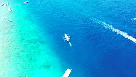 fishing-and-speedboats-floating-in-the-tropical-sea-near-the-coral-reef,-tilting-up