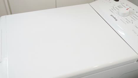 Hands-putting-towels-in-toploader-washing-machine,-opening,-closing-machine
