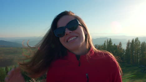 Ein-Glückliches-Mädchen-Lächelt-Und-Steht-Mit-Sonnenbrille-Auf-Einem-Hügel-Mit-Einer-Atemberaubenden-Landschaft-Im-Hintergrund