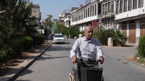 An-old-man-riding-a-bike,-cars-moving-and-people-walking-in-the-outskirts-of-Syria-Damascus