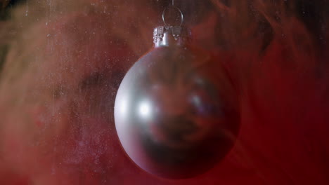 macro-shot-christmas-bauble-with-small-smoke-particals,-which-look-like-snow,-falling-onto-it-in-slow-motion