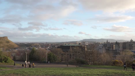 Panning-shot-from-Calton-hill-with-people-walking-and-Nelson-monument-in-the-foreground-with-nice-sunset-light-and-clouds-overlooking-the-city-of-Edinburgh,-Scotland