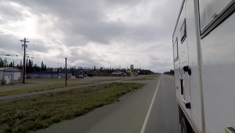 Side-view-of-the-truck-moving-shot,-passing-through-the-cars-and-buildings-of-Tok,-Alaska-on-the-Alaska-Highway